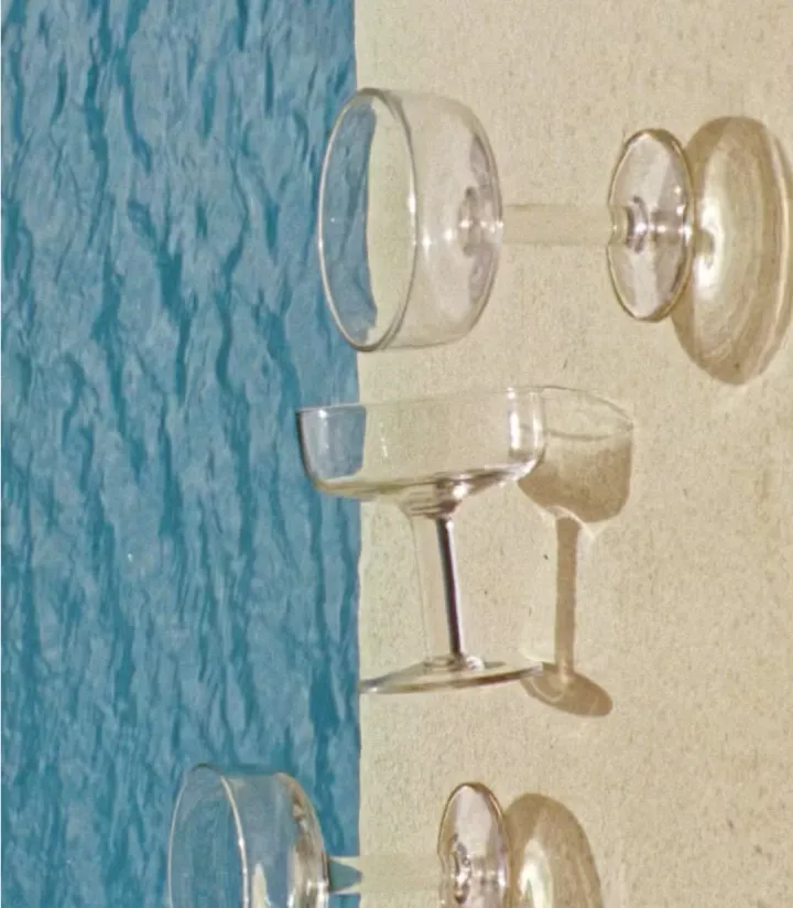 Close-up of vintage coupe and wine glasses against a blue pool and tan wall