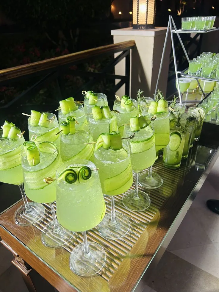 Rows of green cucumber cocktails lined up on a mirrored bar at night