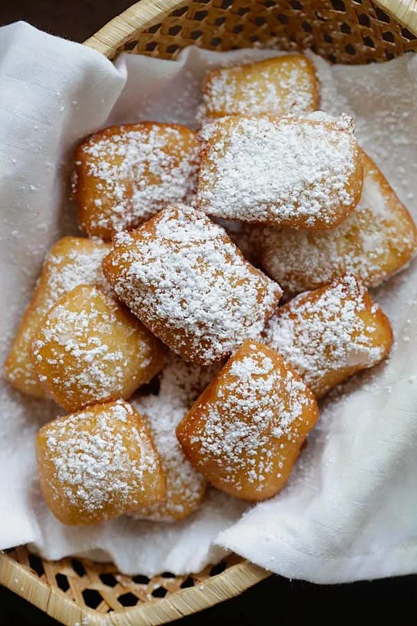 Powdered sugar beignets piled in a cloth-lined basket