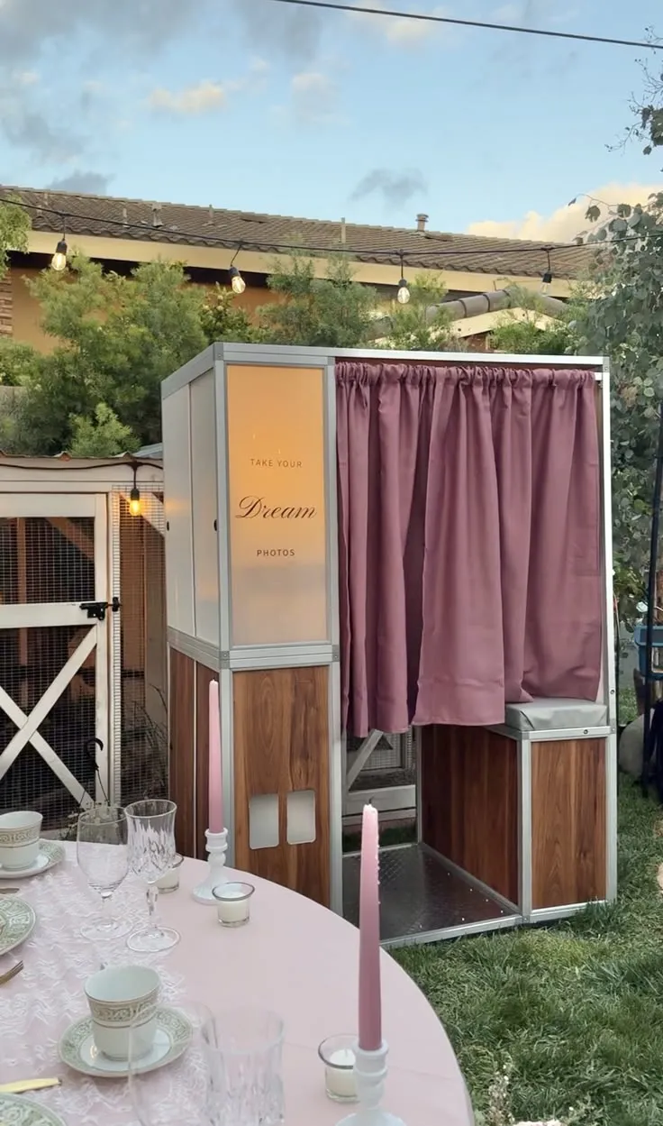 Retro photo booth with a mauve curtain set up beside a pink outdoor table setting
