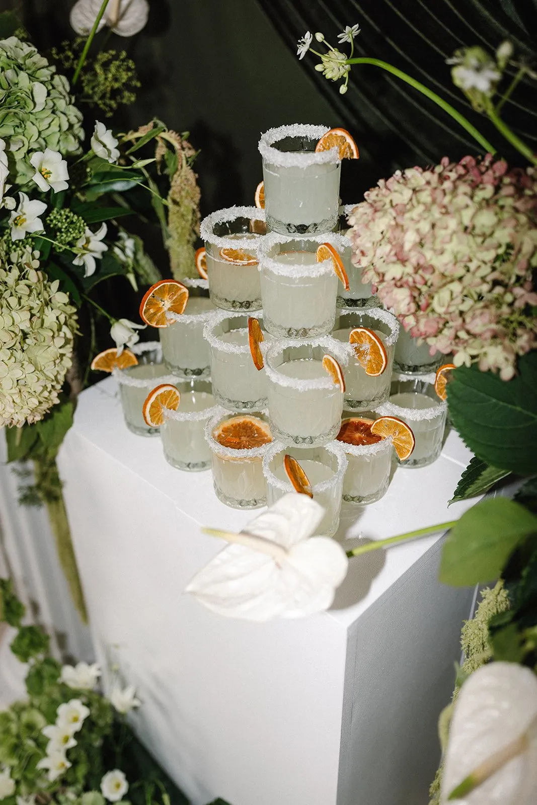 Pyramid of salt-rimmed cocktail shooters garnished with dried orange slices among hydrangeas