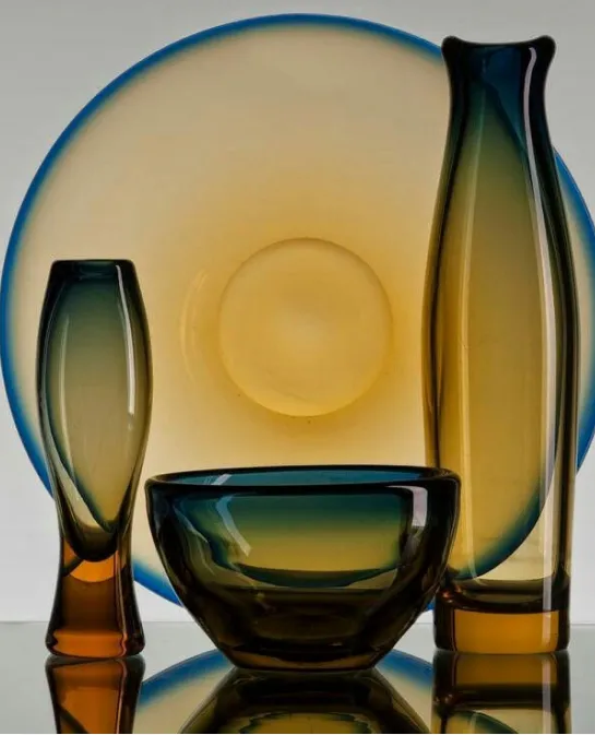Amber and blue glass vessels, including a bowl, vase, and plate, in still life