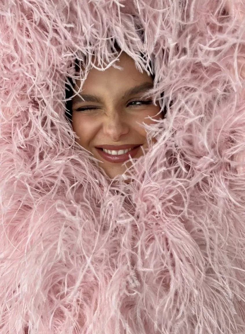 Close-up of a smiling woman peeking through a pink feather hood