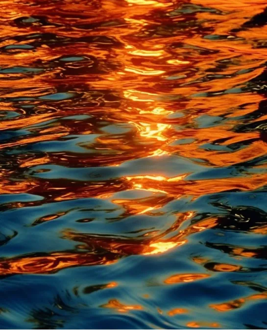 Rippling water reflecting fiery orange sunset light over deep blue