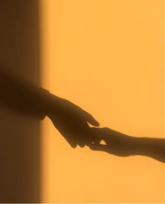 Silhouette of two hands reaching toward each other against a warm orange backdrop